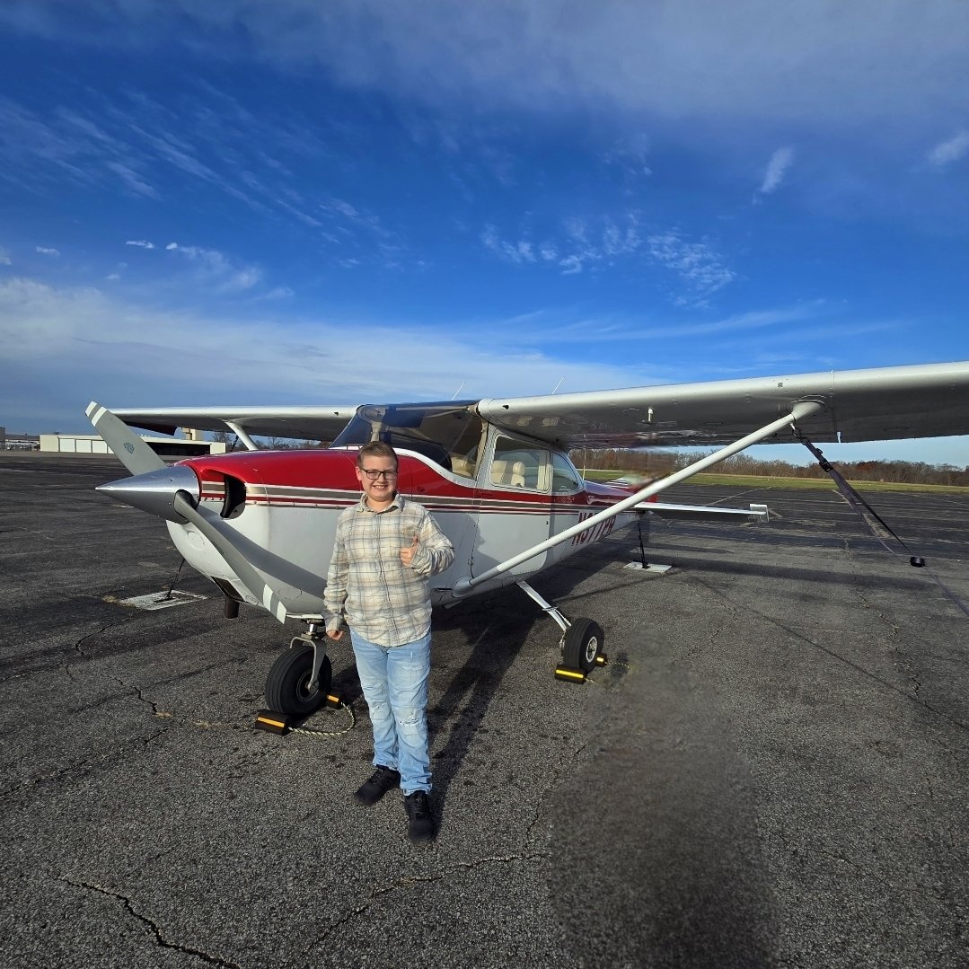 Tayden Franklin standing in front of a red and white Cessna airplane, giving a thumbs up